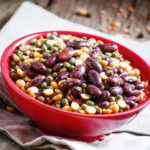 Bean mix: purple beans, green and red lentils, dry peas in a red bowl, vintage wooden background, selective focus