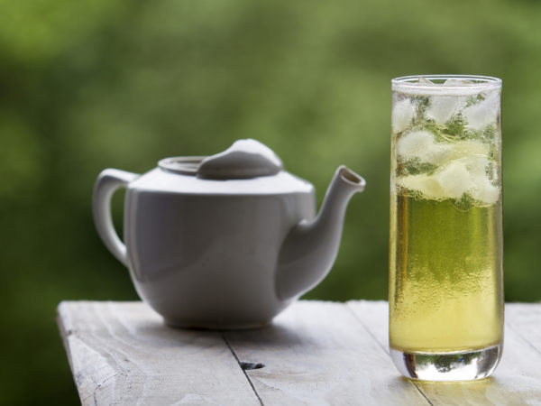 With long green ice tea and glass teapot on unfocused background