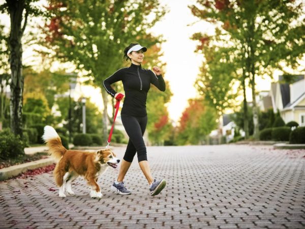 Young woman walking her don in a neighborhood with houses and trees in the background.