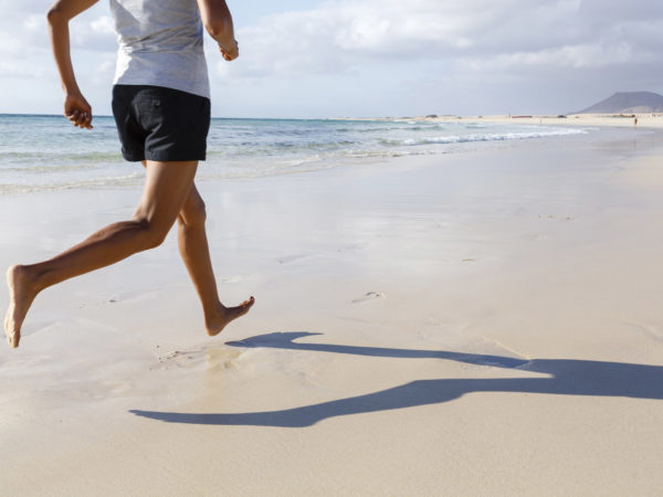 Fit Asian runner jogging on beach barefoot