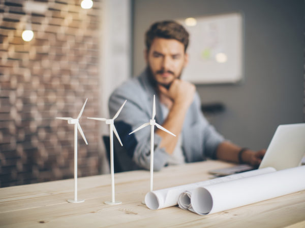 Young engineer at modern office space, sitting at the table and working on energy project.  Focus on wind turbine models on the table.