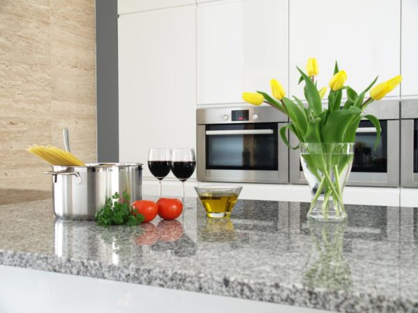 Tomatoes, herbs, wine and flowers on a granite counter top.