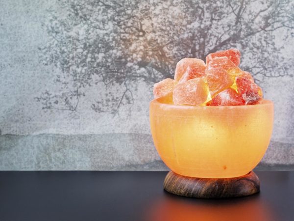 Turned on Himalayan pink salt lamp carved as a bowl on a black table.