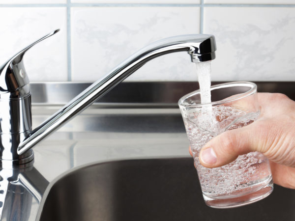 Hand holding a glass of water poured from the kitchen faucet.