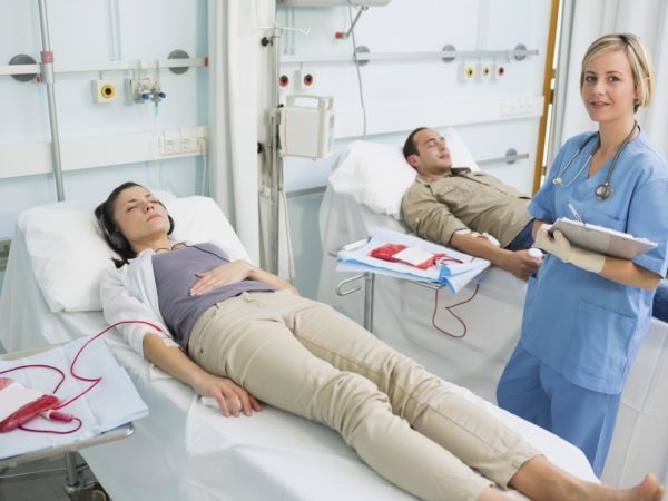 Nurse next to a patient writing on a clipboard in hospital ward