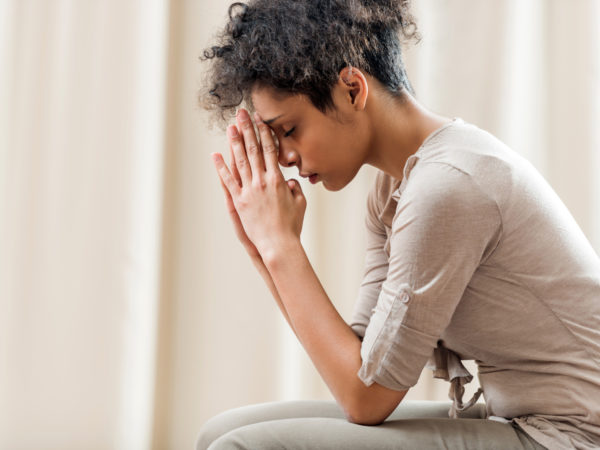 Young African American woman at home praying with her eyes closed.