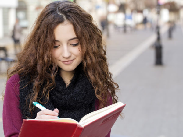 teen school girl writing on a notebook, while standing on walking street