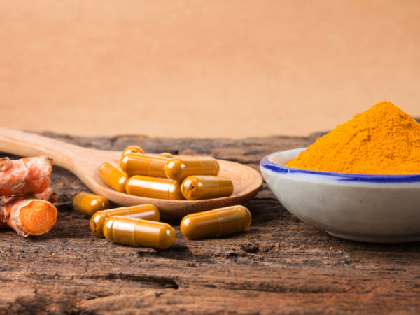 the turmeric powder and capsule and roots curcumin on wooden plate