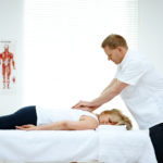 Male osteopath treating back problem of a woman lying on medical room