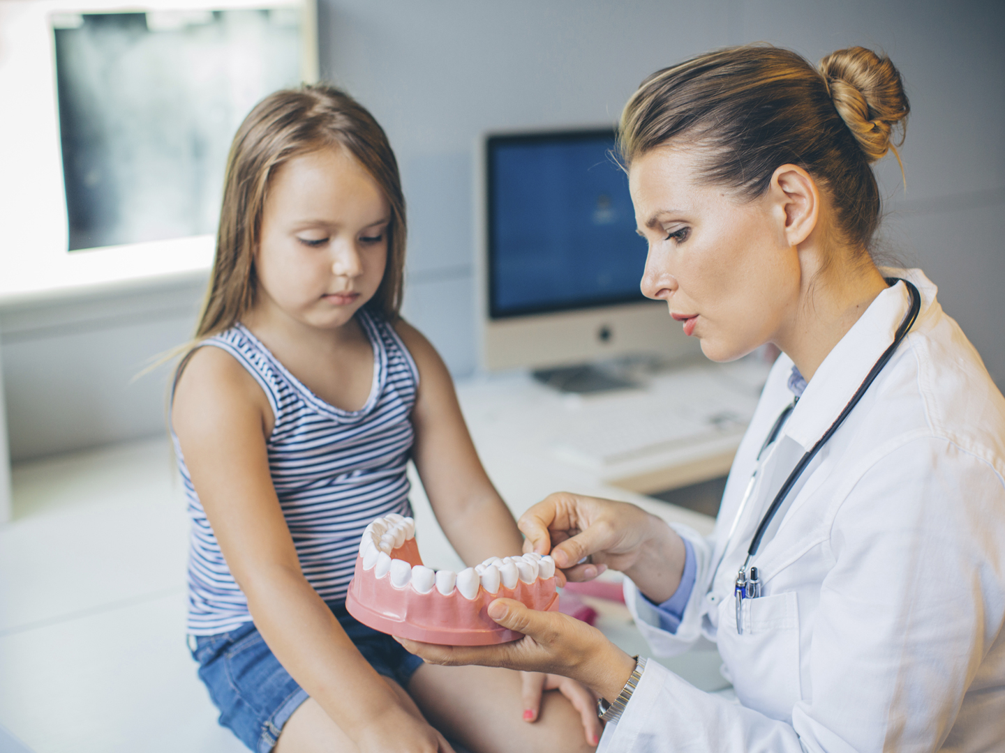 Cute five years old girl visiting doctor&#039;s office. Sitting on the table while doctor teaching her how to take care of teeth. Dental hygiene.