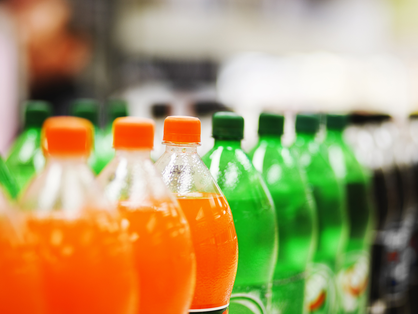 A long line of unbranded soda bottles in various flavours and colors, the focus on the center of the line.