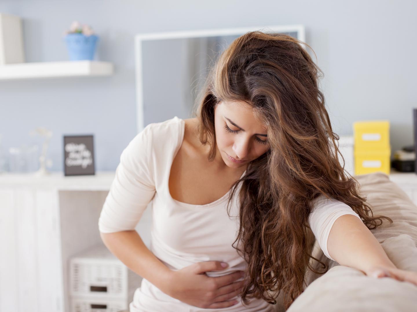 Young woman sitting on the bed with hard stomach pain