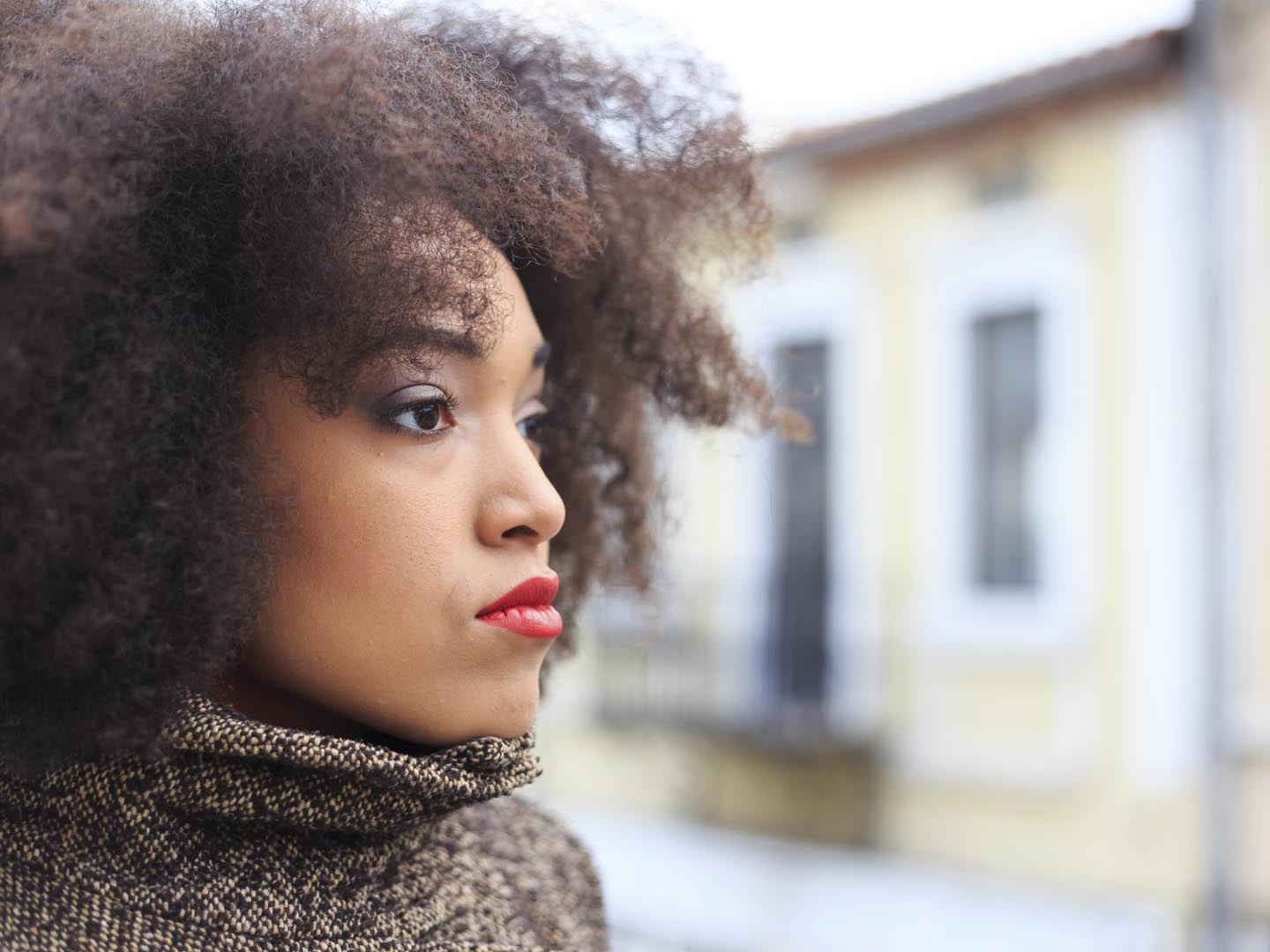 Pensive young woman with gray coat waiting on street. Buildings as background.