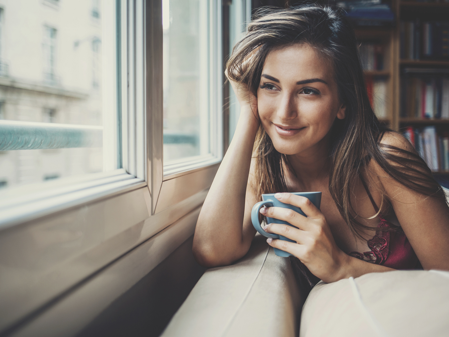 Beautiful young woman holding a cup of coffee looking through a house window. Shot made during Istockalypse Paris 2016 event.