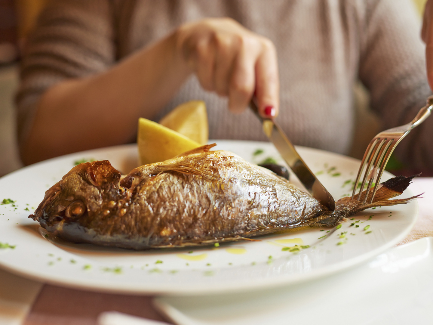 horizontal shot of young woman hands preparing to eat her lunch, fish and lemon in plate.