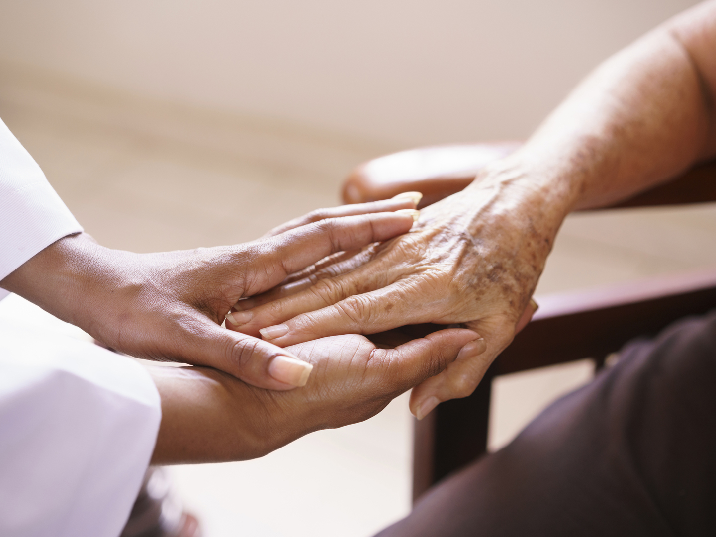 Old people in geriatric hospice: Aged patient receives the visit of a female black doctor. They shake their hands and talk in the hospital.