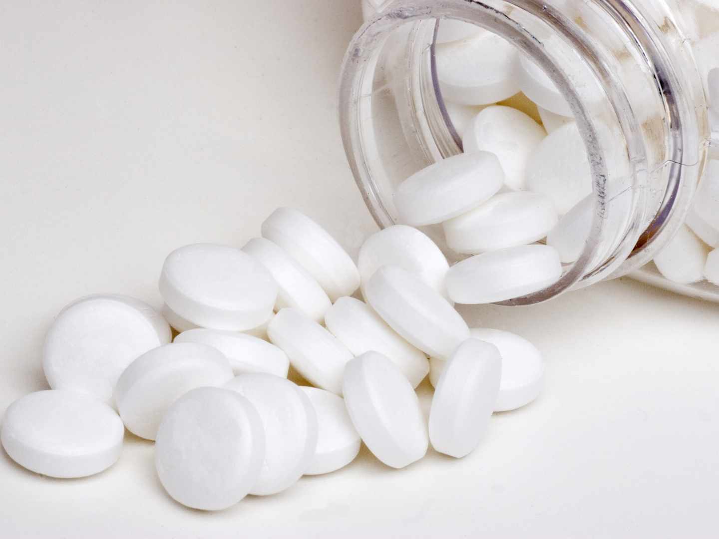 Multiple aspirin pills being poured from the mouth of a pill bottle.