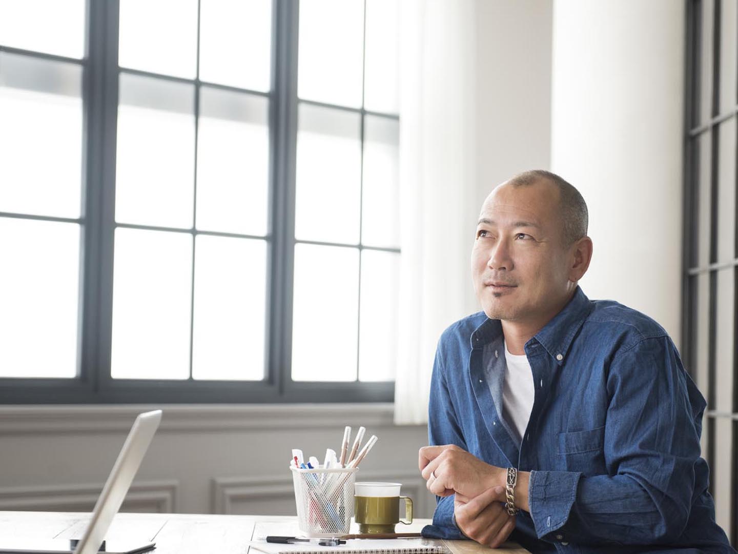 Thoughtful Japanese man looking for inspiration and creativity. Pensive Asian businessman looking away from desk