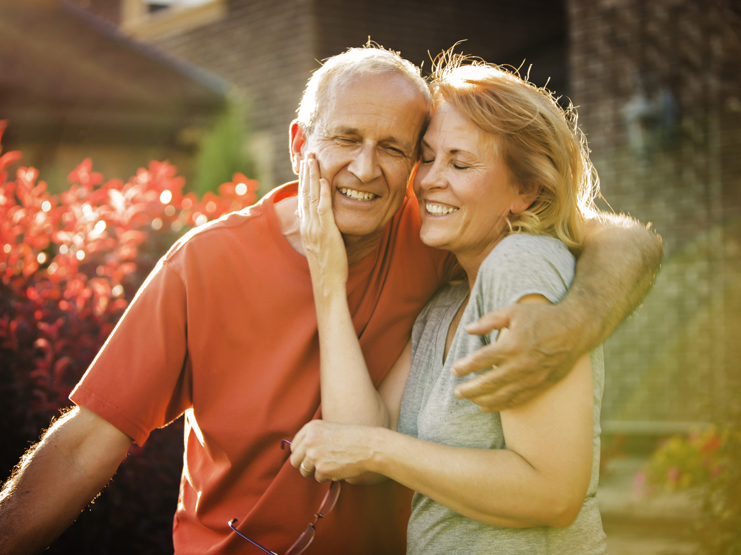 Mature couple hugging each other outside in front of their home.