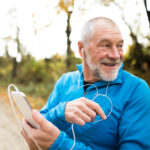 Senior runner in nature. Man with smart phone, listening to classical music.