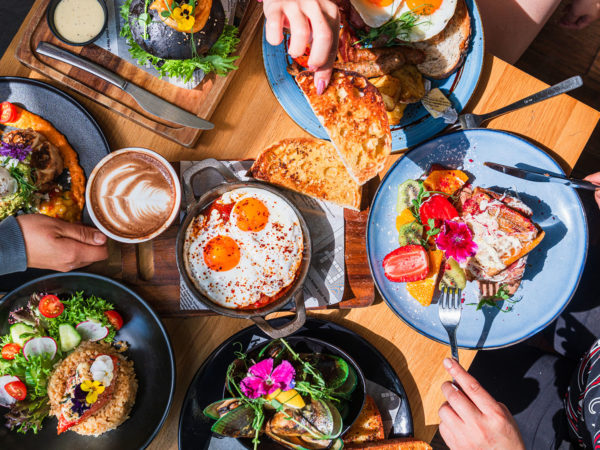 Table top view of breakfast food displayed on table, people eating food.